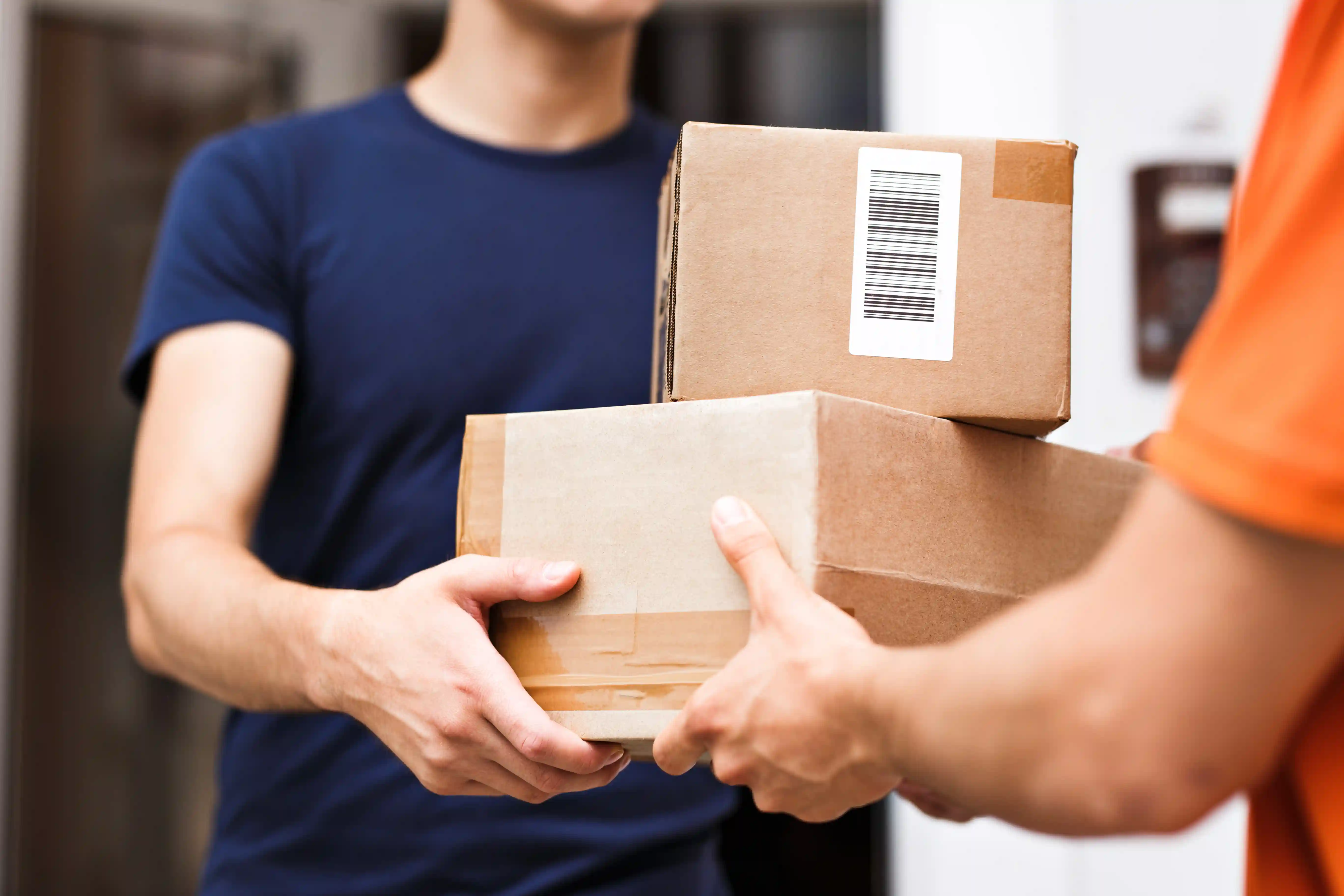 Mann in blauem T-Shirt nimmt zwei Kartons von einer anderen Person entgegen, Nahaufnahme einer Paketübergabe.